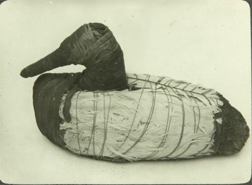 A vintage decoy duck made of natural materials, featuring a wrapped body and a pointed beak.