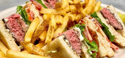 A plate of sandwiches with pink beef patties, lettuce, and tomato, served with golden French fries.