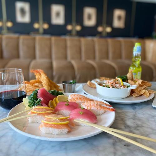 A table setting with sushi, shrimp, a salad, and a glass of red wine, against a stylish background.