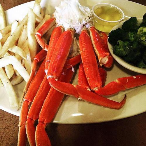 A plate with crab legs, fries, broccoli, and a small cup of dipping sauce.