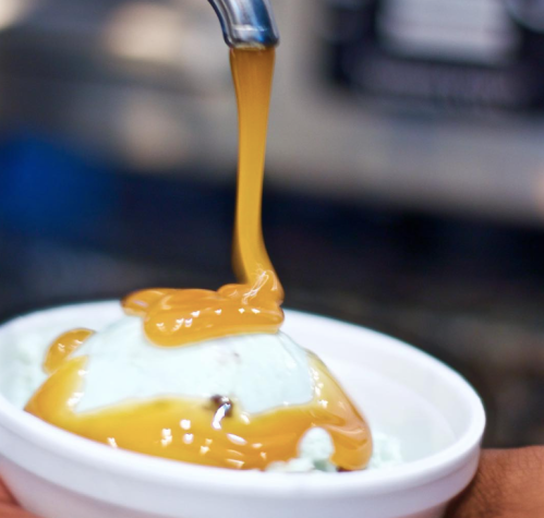 A scoop of mint ice cream topped with a drizzle of golden syrup in a white bowl.