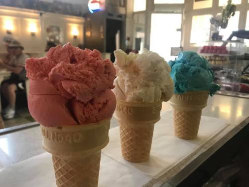 Three ice cream cones with pink, white, and blue scoops, displayed on a counter in a cozy ice cream shop.
