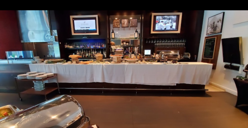 A modern bar setup with a buffet table, drinks, and two screens displaying information in a stylish interior.