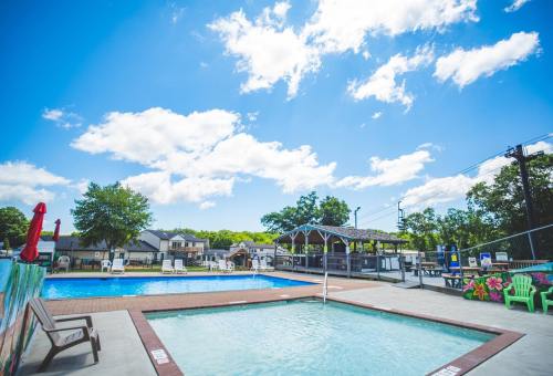 A sunny pool area featuring two pools, lounge chairs, and a gazebo under a blue sky with fluffy clouds.