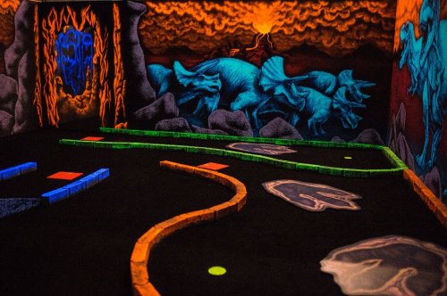 A glow-in-the-dark mini-golf course featuring dinosaur murals and colorful pathways.