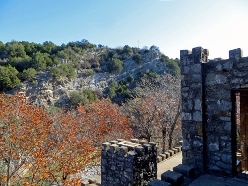 A stone wall overlooks a rocky hillside with trees and autumn foliage under a clear blue sky.