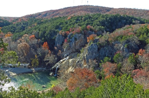 A scenic view of a waterfall cascading into a green pool, surrounded by colorful autumn foliage and rocky hills.
