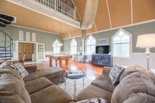 Cozy living room with a spiral staircase, pool table, and large windows, featuring a modern design and warm colors.