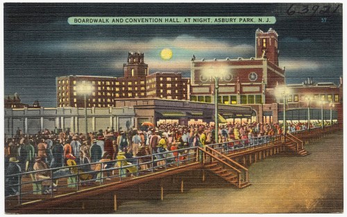 A vibrant night scene of a boardwalk and convention hall in Asbury Park, NJ, bustling with people under a full moon.