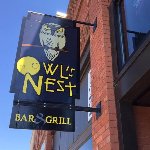 Sign for "Owl's Nest Bar & Grill" featuring an owl graphic, mounted on a brick building.