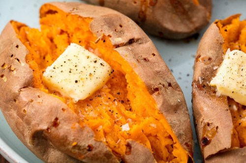 Baked sweet potatoes topped with a pat of butter and sprinkled with black pepper on a light blue plate.