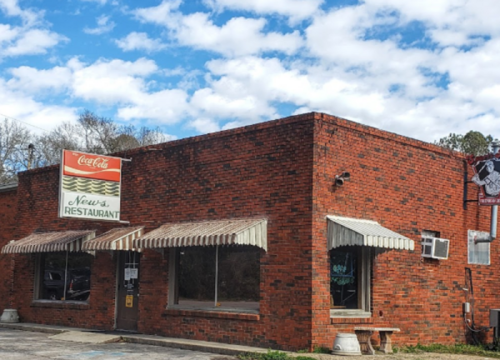 A brick restaurant building with a Coca-Cola sign and striped awnings under a blue sky with clouds.