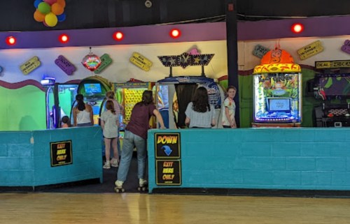 A colorful roller skating rink with arcade games and children enjoying the activities.