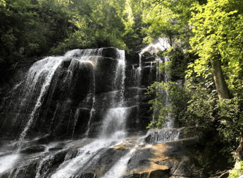A serene waterfall cascading over rocky terrain, surrounded by lush green trees and sunlight filtering through the leaves.