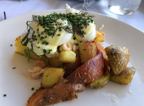 A plate of eggs Benedict with poached eggs, herbs, and a side of roasted potatoes and vegetables.