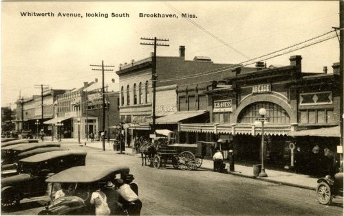 Historic street view of Whitworth Avenue in Brookhaven, Mississippi, featuring vintage cars and storefronts.