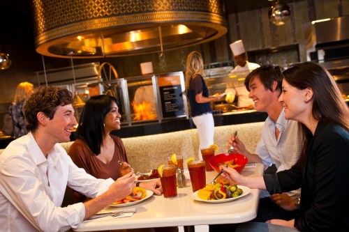 Four friends enjoy a meal together at a restaurant, smiling and sharing food in a lively atmosphere.