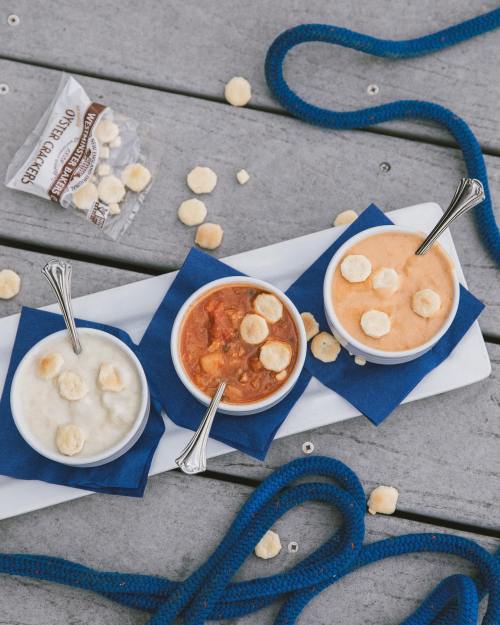 Three bowls of colorful desserts topped with banana slices, arranged on a white platter with blue napkins and a rope background.