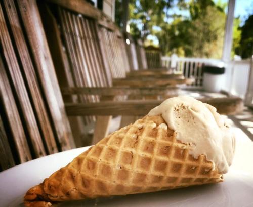 A close-up of a waffle cone with a scoop of ice cream, set on a plate with wooden chairs in the background.
