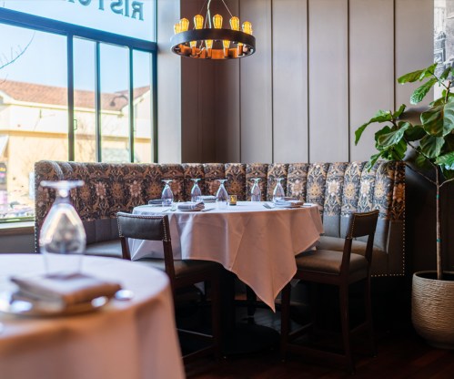 Cozy restaurant booth with a round table, elegant decor, and a large window letting in natural light.