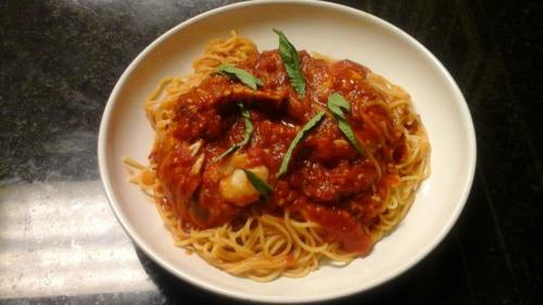 A bowl of spaghetti topped with marinara sauce and fresh basil leaves on a dark countertop.