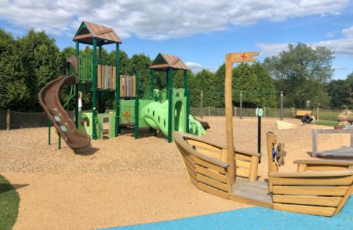 A colorful playground featuring a slide, climbing structures, and a wooden boat, set on a sandy surface.