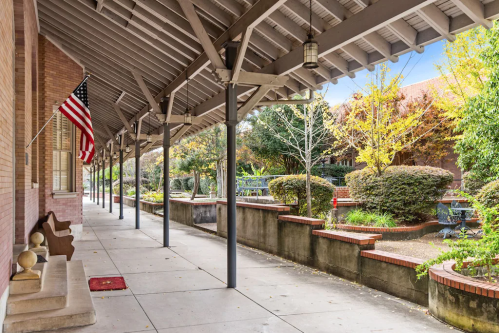 A covered walkway with an American flag, surrounded by greenery and a peaceful garden area.