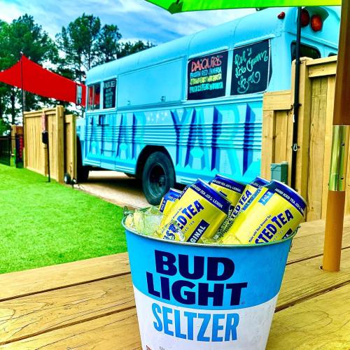 A bucket of Bud Light Seltzer sits on a wooden table, with a colorful food truck in the background.