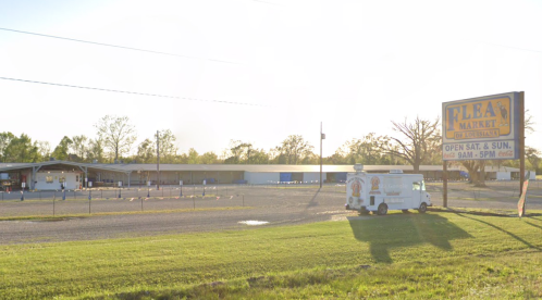 A sunny view of a flea market with a sign, open on weekends, and a food truck parked nearby.