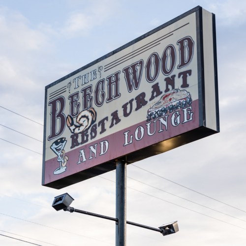 Sign for Beechwood Restaurant and Lounge featuring a martini glass and a classic car, set against a cloudy sky.