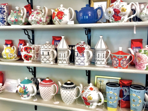 A display of colorful teapots on shelves, featuring various designs and patterns, alongside decorative mugs.