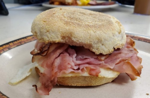 A close-up of a sandwich with layers of ham and an egg on a toasted English muffin.