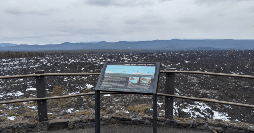 View from a lookout point featuring a sign about nearby glaciers, with a vast, rocky landscape and mountains in the distance.