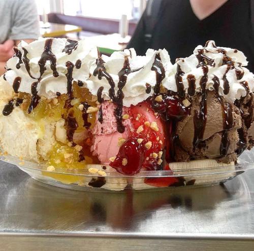 A colorful ice cream sundae with scoops of various flavors, topped with whipped cream, chocolate sauce, and cherries.