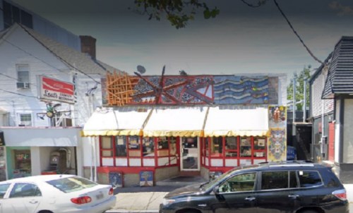 Colorful restaurant exterior with a mural, awning, and parked cars in front.