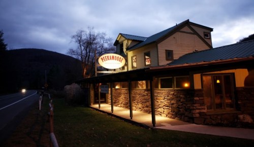 A rustic building with a sign reading "Peekamoose," set against a twilight sky and surrounded by trees.