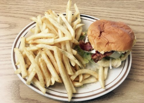 A plate with a burger topped with lettuce and bacon, accompanied by a generous serving of French fries.