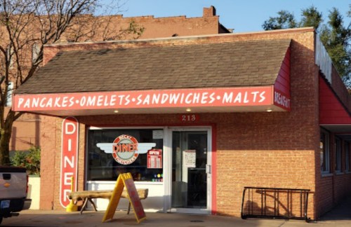 A brick diner with a red awning displaying "Pancakes, Omelets, Sandwiches, Malts" above the entrance.