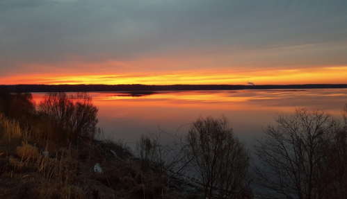 A serene sunset over a calm lake, with vibrant orange and yellow hues reflecting on the water's surface.