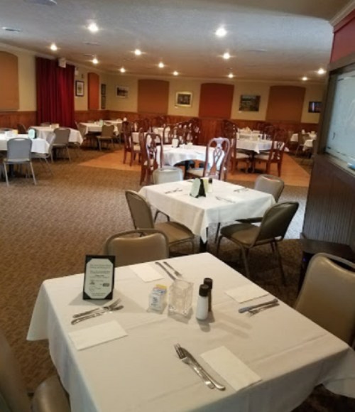 A spacious restaurant with neatly set tables, white tablecloths, and a cozy atmosphere.