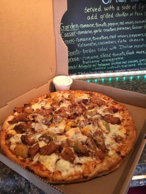 A pizza topped with grilled chicken, cheese, and vegetables, served in a pizza box with a side of dipping sauce.