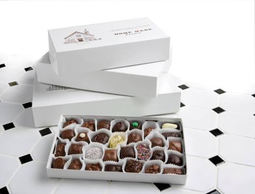 A white box of assorted chocolates displayed on a tiled surface, with two empty boxes stacked in the background.