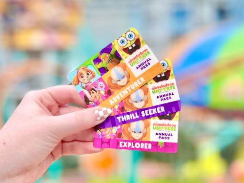 A hand holding three colorful Nickelodeon theme park annual pass cards labeled "Adventurer," "Thrill Seeker," and "Explorer."