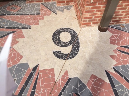 A mosaic floor featuring a large black number 9 surrounded by colorful geometric patterns.