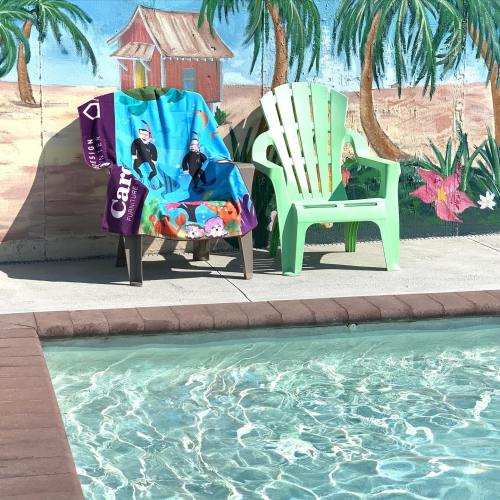 Two colorful chairs by a pool, with a tropical mural of palm trees and a house in the background.
