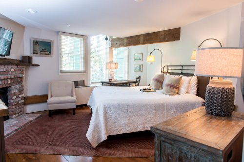 Cozy bedroom with a fireplace, large windows, a bed with decorative pillows, and rustic wooden accents.