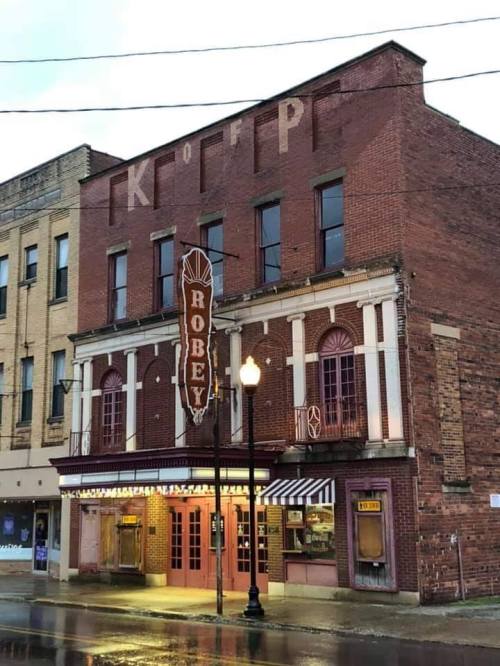 Historic brick building with "Robey" marquee, featuring arched windows and a vintage theater entrance. Rainy street scene.