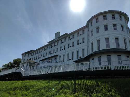 A large, white, multi-story building with a curved design, set against a clear blue sky and sun. Green grass in the foreground.