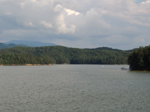 A serene lake surrounded by lush green hills under a cloudy sky.