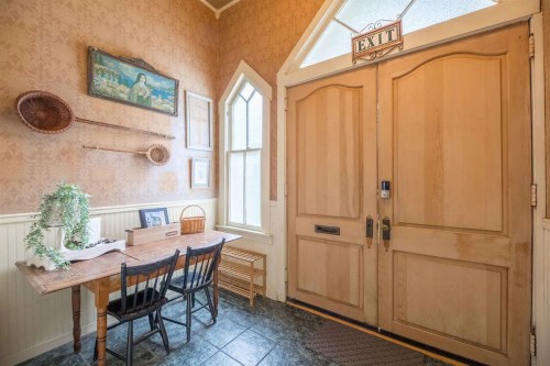 A cozy entryway with wooden doors, a table, chairs, and decorative wall art in warm tones.